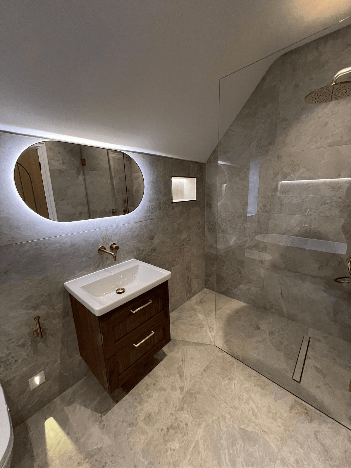 Grey stone bathroom with backlit mirror and walk-in shower
